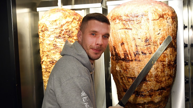 Fußball-Weltmeister Lukas Podolski steht am 06.01.2018 in Köln (Nordrhein-Westfalen) bei der Eröffnung eines Döner-Ladens an einem Dönerspieß.