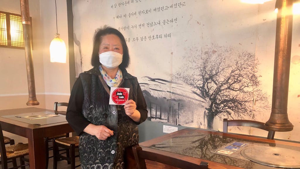 Die Inhaberin des koreanischen Restaurants Nakwon, Joeng Sook Choe Lee, hält das Jode Lade-Gütesiegel in die Kamera.