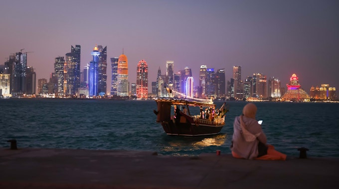 Eine Frau schaut auf ihr Smartphone vor der Skyline von West Bay Doha in Katar