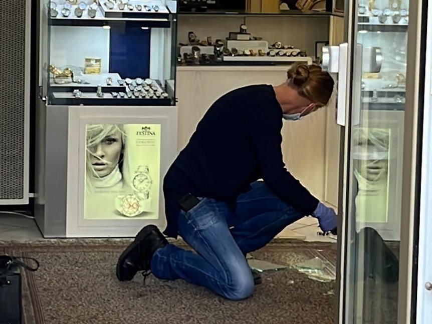 Ein Mann kniet in einem Kölner Juwelier-Geschäft auf dem Boden vor einem Haufen Scherben. Der Laden wurde kurz zuvor ausgeraubt.