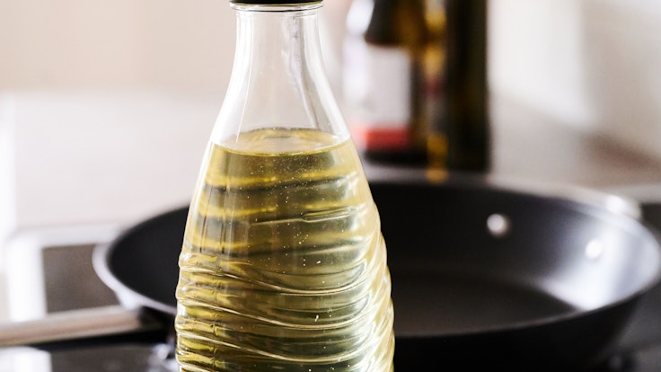 In eine Glasflasche abgefülltes Sonnenblumenöl steht neben einer Pfanne in einer Küche. Die Nachfrage nach Speiseöl und Mehl in Deutschland ist nach Beginn des Ukraine-Krieges zeitweise stark gestiegen.