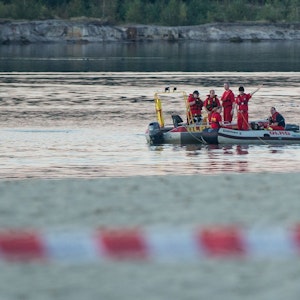 Einsatzkräfte der Feuerwehr und des DLRG fahren in Booten auf einem See.