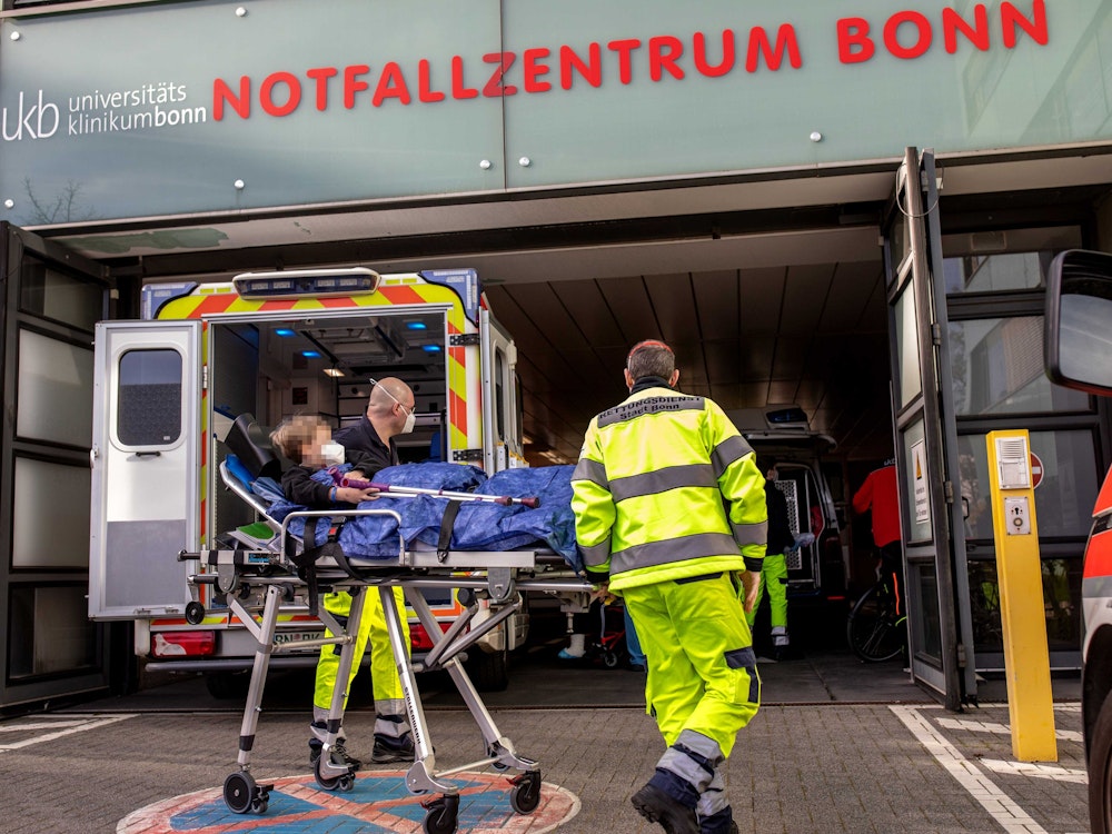 Zwei Männer bringen ein kleines Kind auf einer rollenden Krankentrage in das Notfallzentrum Bonn.