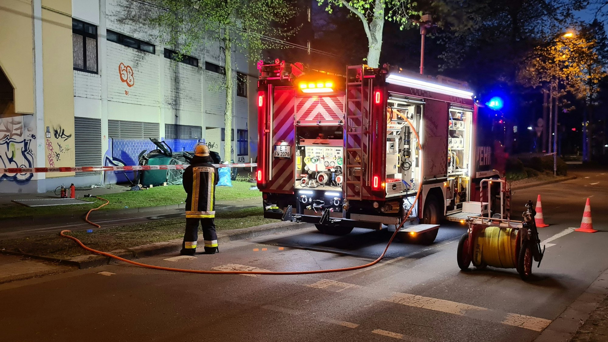 Ein Feuerwehrmann steht neben dem Wrack einesAutos. Zwei junge Männer sind am Ostersonntag in Essen mit einem Auto aus der obersten Etage eines Parkhauses gestürzt und ums Leben gekommen.