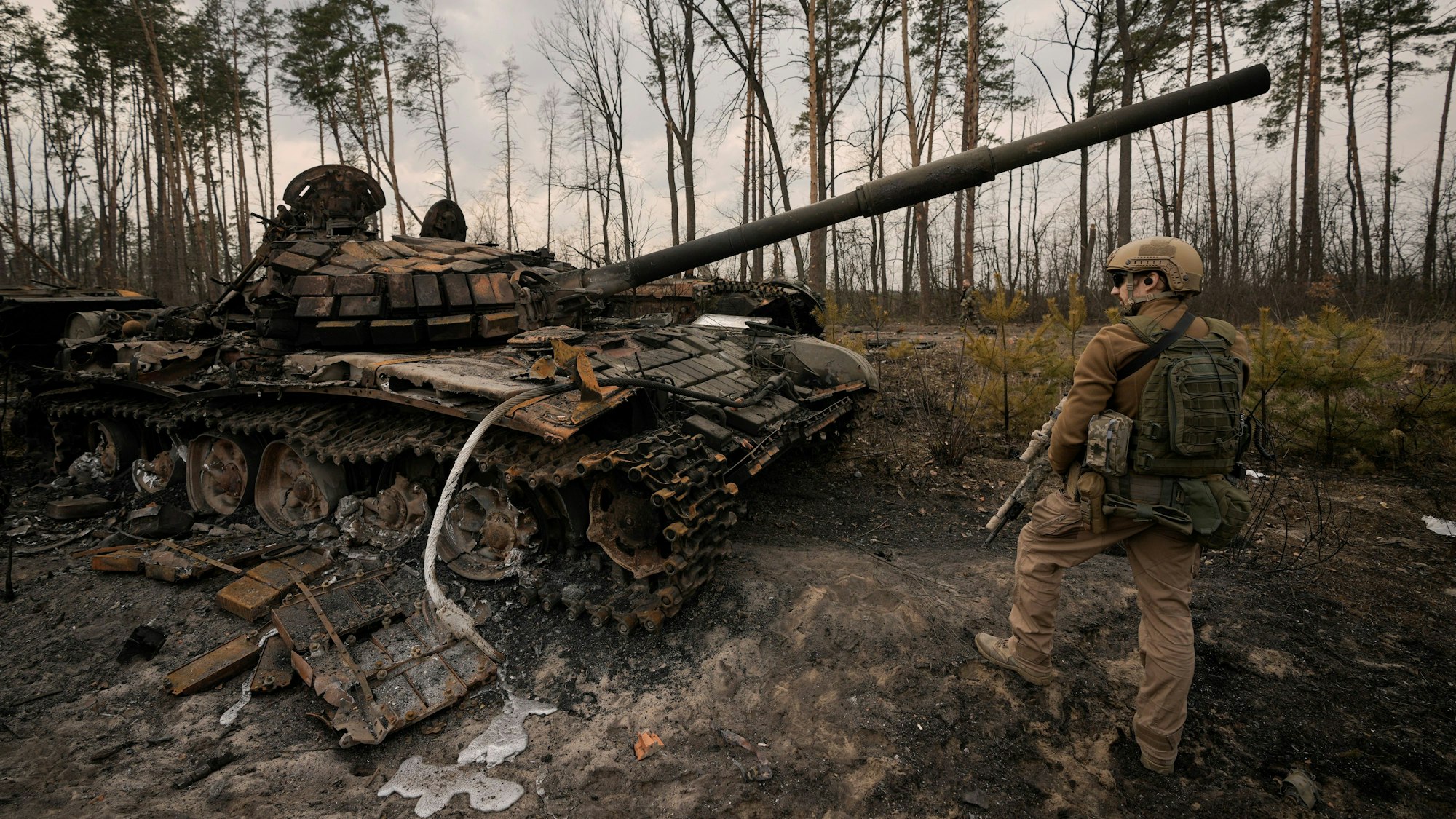 Ein ukrainischer Soldat steht am Stadtrand von Kyjiw neben einem zerstörten Panzer.