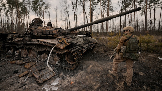 Ein ukrainischer Soldat steht am Stadtrand von Kyjiw neben einem zerstörten Panzer.