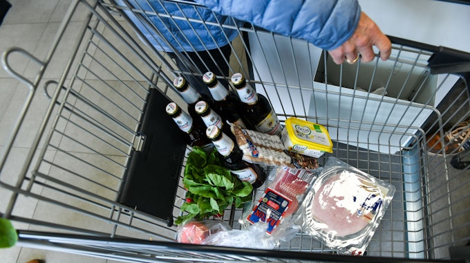 Ein Kunde hat Bier, Wurst, Margarine, Schinken und Salat in einen Einkaufswagen gelegt.
