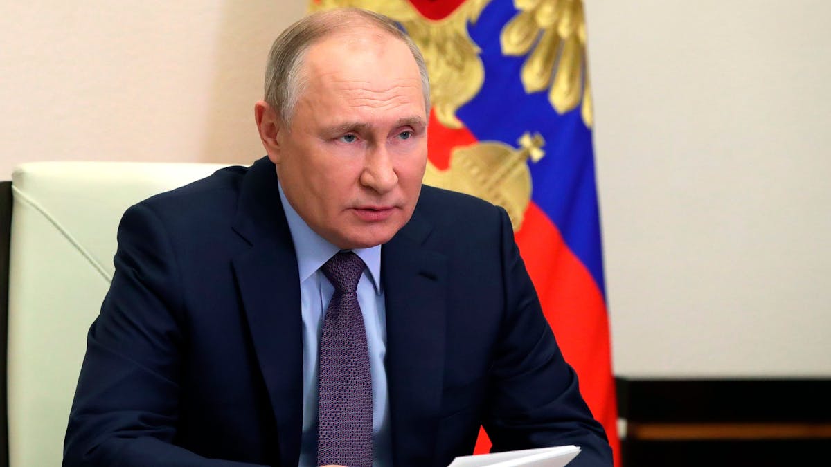 Wladimir Putin sitzt an einem Schreibtisch. Hinter ihm hängt die russische Flagge.