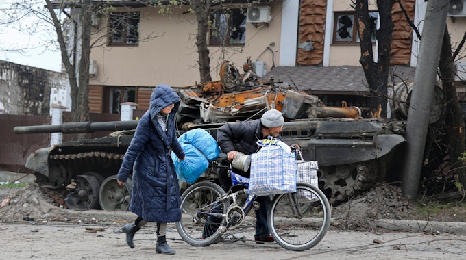 Zwei Personen laufen durch die Kriegstrümmer. Im Hintergrund ist ein zerstörter Panzer zu sehen.