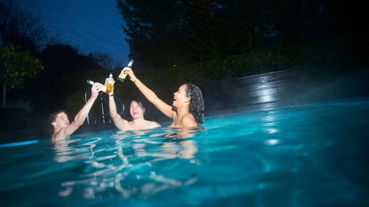 Drei Menschen stoßen in einer Werbung für Gaffel mit Flaschen in einem Swimming Pool an.