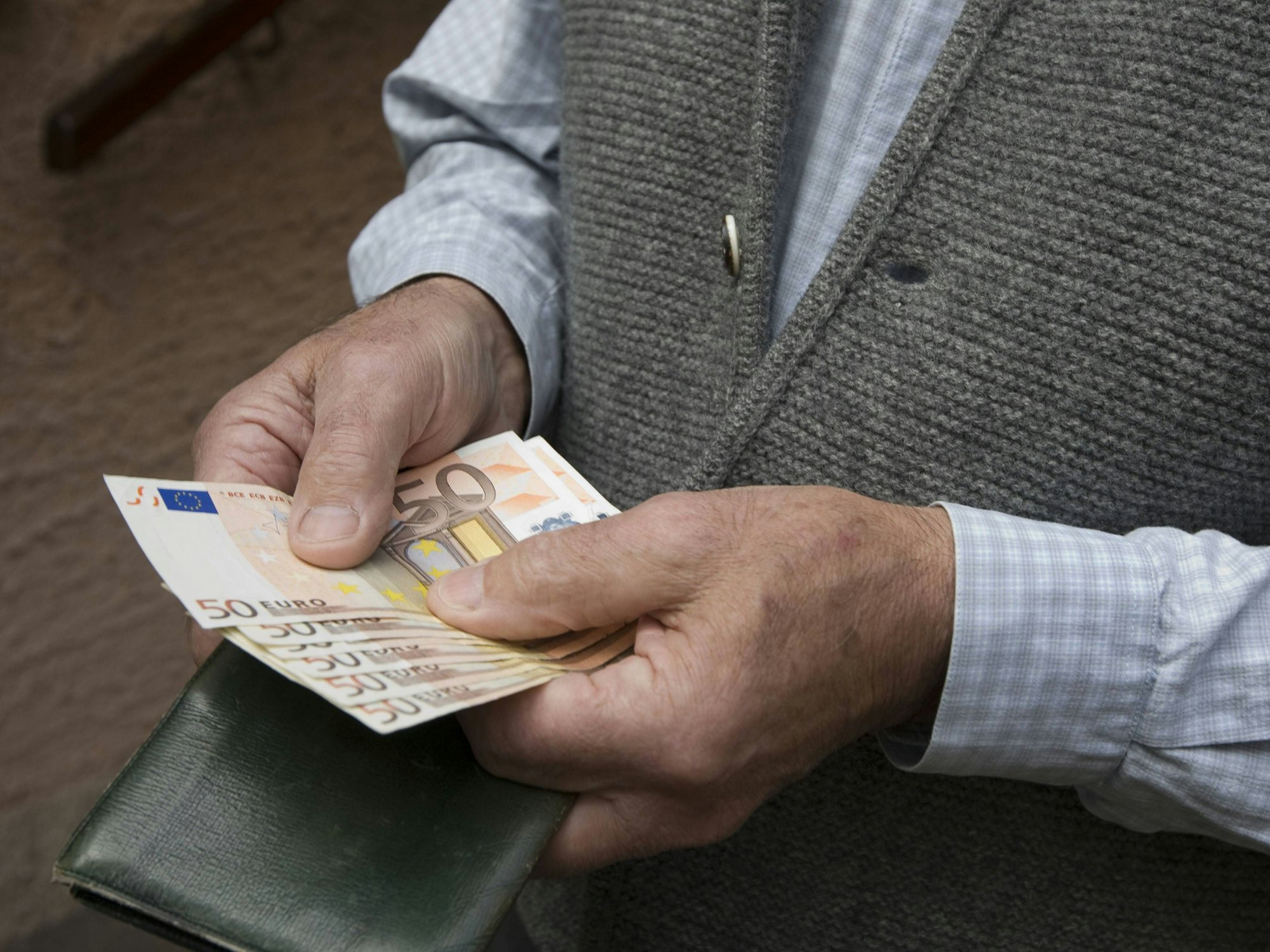 Ein Senior hält mehrere 50-Euro Scheine in den Händen.