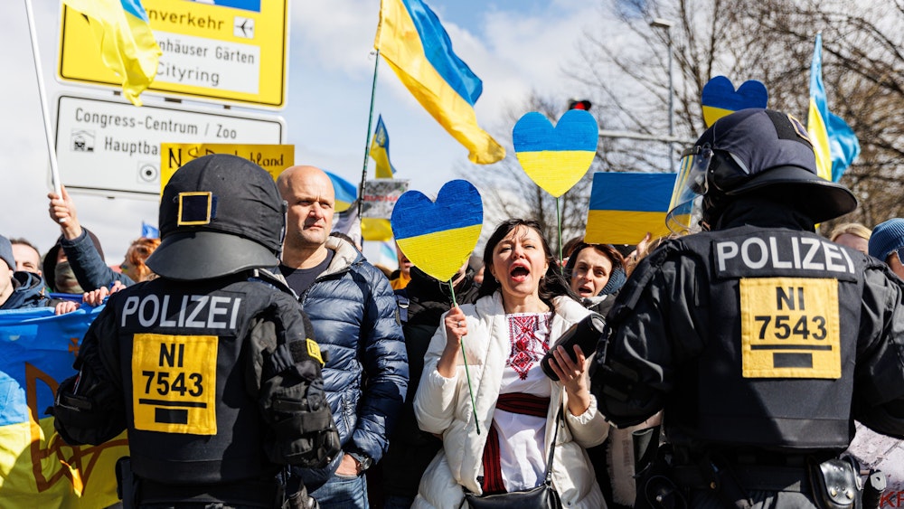Menschen mit Ukraine-Fahnen werden von Polizisten bewacht.