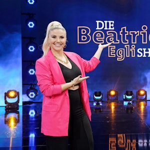 Beatrice Egli zeigt auf das neue Logo ihrer Schlagershow „Die Beatrice Egli Show“.