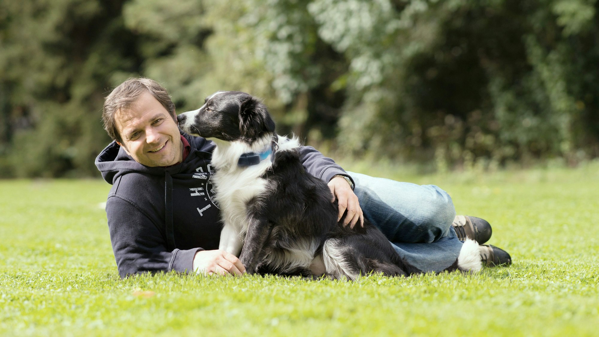 Martin Rütter liegt neben einem Hund auf einer Wiese.