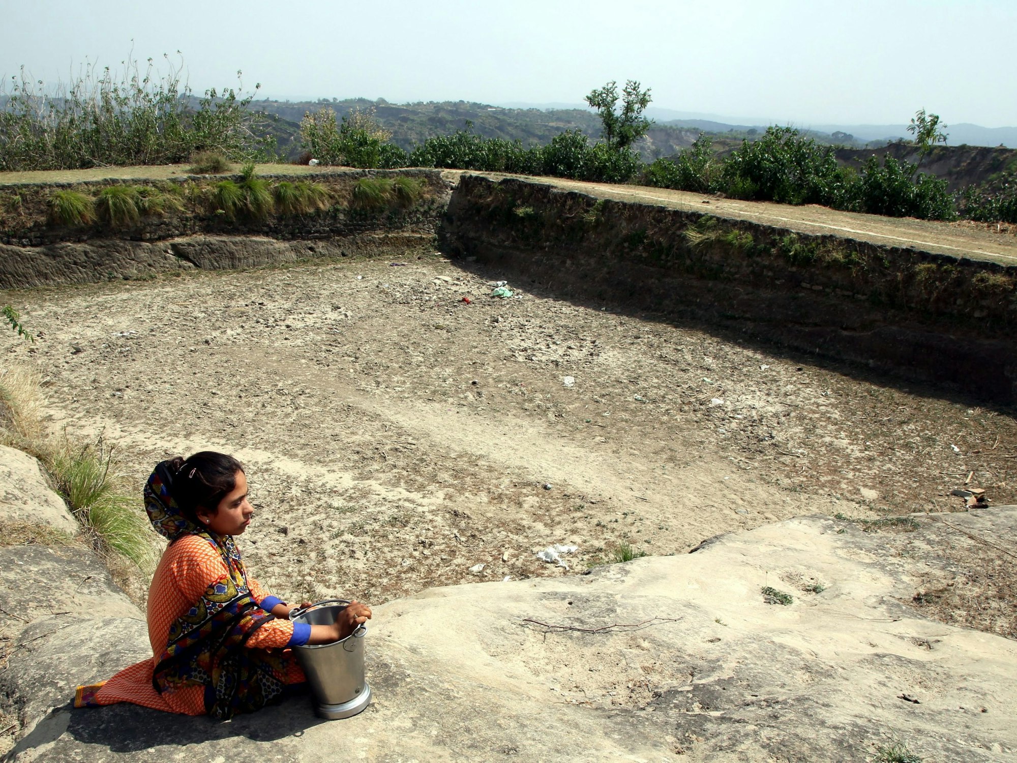 Eine Frau auf der Suche nach Trinkwasser sitzt am ausgetrockneten Speicherbecken.