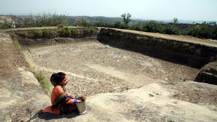 Eine Frau auf der Suche nach Trinkwasser sitzt am ausgetrockneten Speicherbecken.