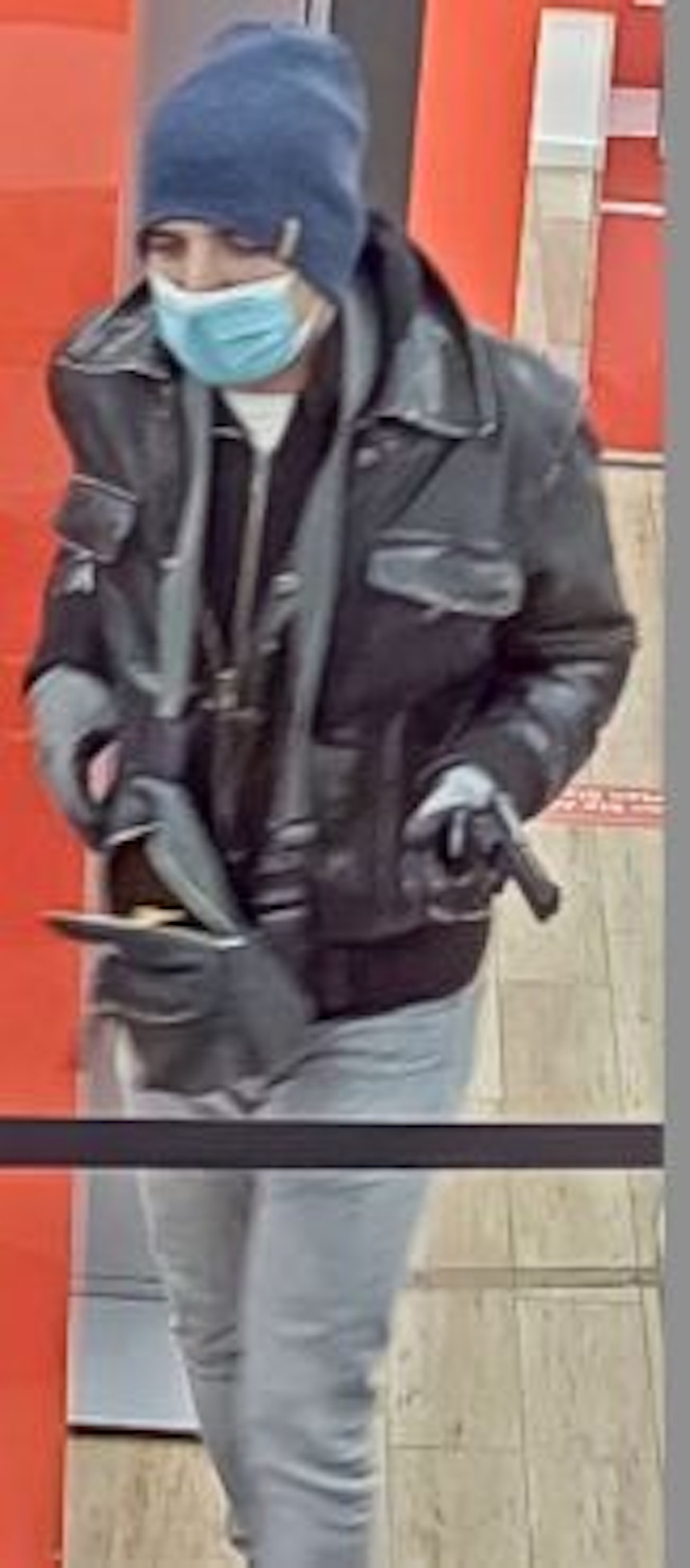 Ein Mann hält eine Pistole in der Hand und hat seine Mütze bis tief ins Gesicht gezogen.