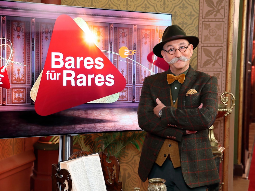 Moderator Horst Lichter steht neben dem Logo der Sendung Bares für Rares.