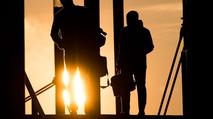 Auf dem Symbolfoto gehen zwei Männer mit Aktentasche bei Sonnenaufgang über eine Brücke an der Expo Plaza.