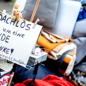 Ein Schild mit der Aufschrift „Obdachlos - bitte um eine Spende - danke!“ steht neben den Habseligkeiten eines Obdachlosen, die auf einem Bürgersteig in der Innenstadt liegen.