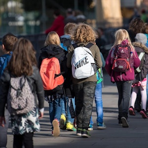 Schulkinder mit Rucksäcken gehen auf einer Straße.