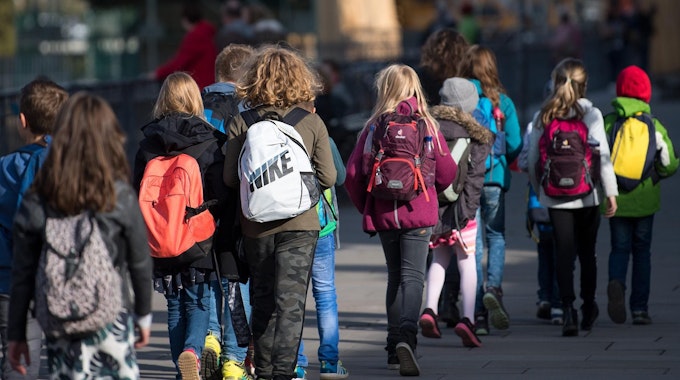 Schulkinder mit Rucksäcken gehen auf einer Straße.