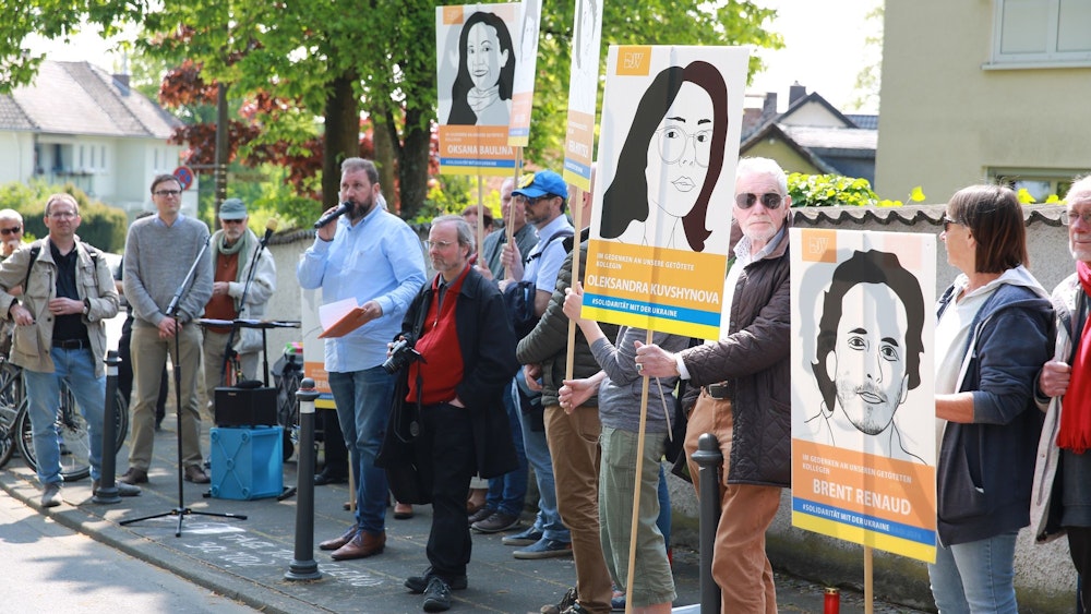 Menschen stehen vor dem russischen Generalkonsulat in Bonn, einige halten die Portraits getöteter Journalistinnen und Journalisten hoch.