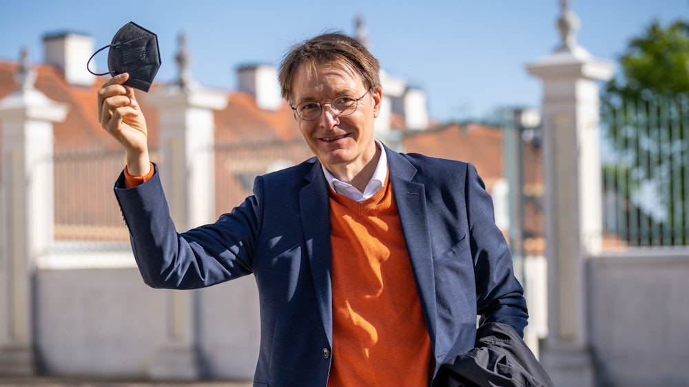 Der Bundesgesundheitsminister Karl Lauterbach (SPD) lächelnd mit erhobener Hand und einer Maske in der Hand am 3. Mai 2022 in Brandenburg.