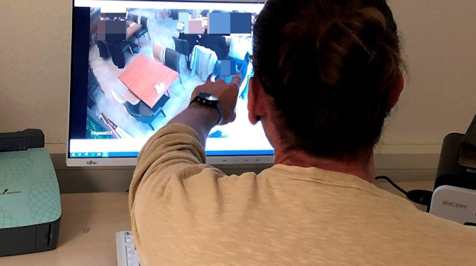 Polizist Niklas B. (39, Name geändert) sitzt vor einem Computerbildschirm und zeigt auf eine Person, die dort auf einem Überwachungsbild zu sehen ist.
