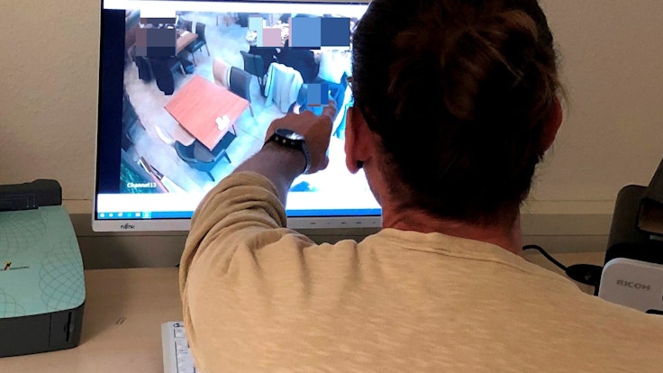 Polizist Niklas B. (39, Name geändert) sitzt vor einem Computerbildschirm und zeigt auf eine Person, die dort auf einem Überwachungsbild zu sehen ist.