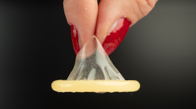 Ein Kondom wird mit zwei Fingern gehalten.