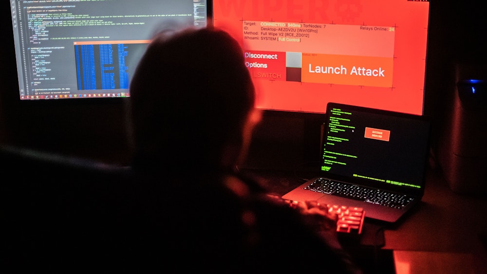 Das Symbolfoto vom 25.02.2022 aus Bad Oeynhausen (NRW) zeigt einen Mann vor Bildschirmen, die Hacker-Programme und eine fiktive Fernlösch-Software zeigen.