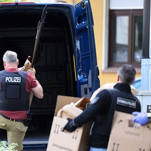 Polizisten tragen Gegenstände, darunter mehrere Stichwaffen und Speere, aus dem Wohnhaus des Verdächtigen.