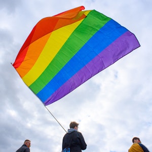 Teilnehmerinnen und Teilnehmer der Kundgebung des Bündnisses „#unteilbar Sachsen-Anhalt“ stehen mit einer wehenden Regenbogenfahne auf dem Domplatz.