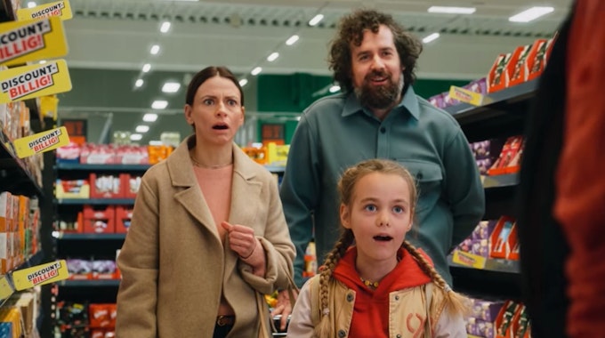 Eine Frau, ein Mann und ein Kind stehen mit aufgerissenem Mund in einem Supermarkt-Gang.