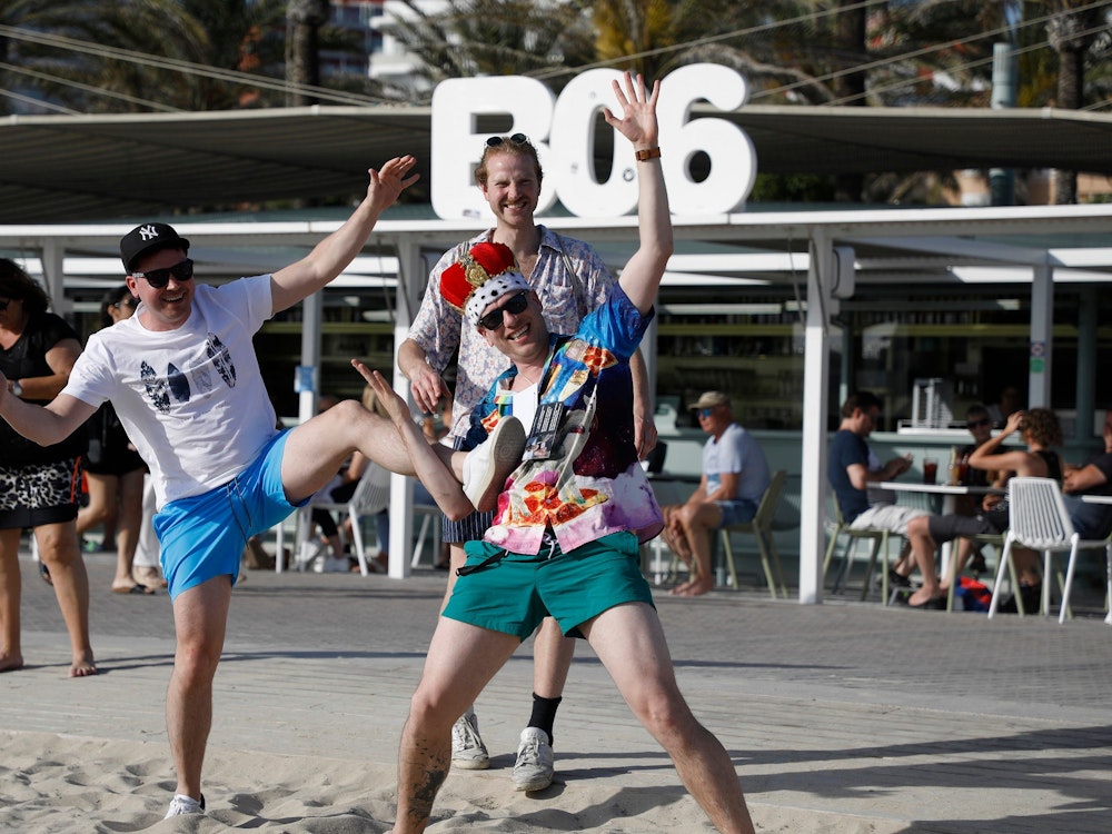 Drei Männer feiern am 13. Mai 2022 am Ballermann-Strand, einer trägt eine Stoff-Krone auf dem Kopf.
