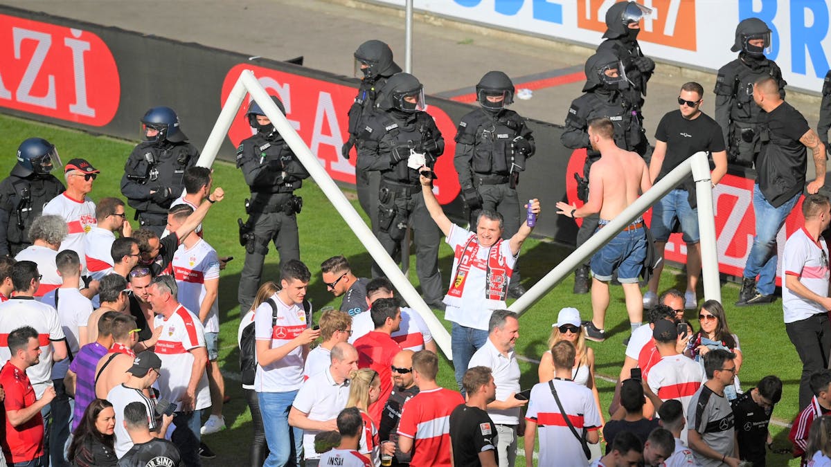 Zahlreiche Fans stehen nach dem Platzsturm vor dem inzwischen gebrochenen Tor auf dem Rasen des VfB Stuttgart. Im Hintergrund zahlreiche Polizeikräfte.