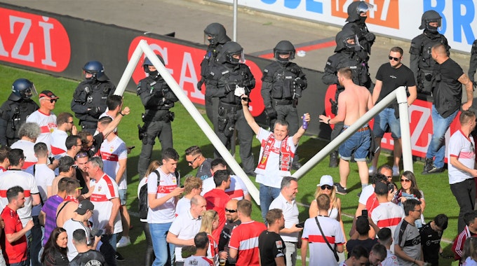 Zahlreiche Fans stehen nach dem Platzsturm vor dem inzwischen gebrochenen Tor auf dem Rasen des VfB Stuttgart. Im Hintergrund zahlreiche Polizeikräfte.