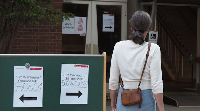 Eine Frau wartet am 15. Mai 2022 mit ihren Wahlunterlagen vor einem Wahllokal in Köln. Maskenpflicht gilt aber nicht.
