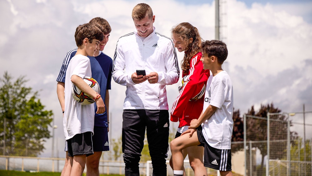 Toni Kroos schaut mit Kindern auf sein Handy.