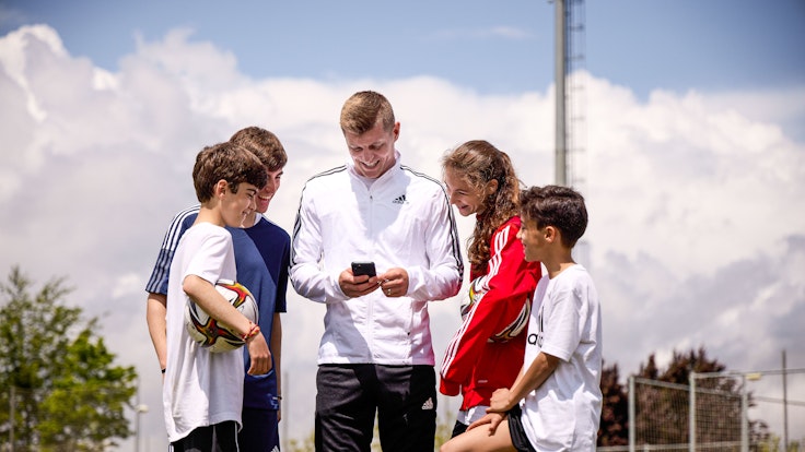 Toni Kroos schaut mit Kindern auf sein Handy.