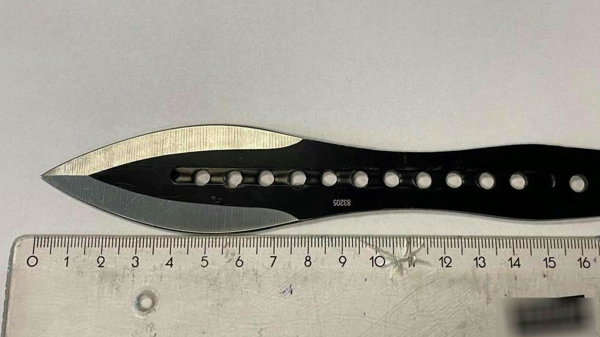 Das schwarze Wurfmesser liegt neben einem Lineal und hat eine knapp acht Zentimeter lange Klinge.