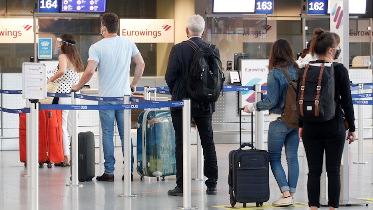 Fluggäste mit Masken warten am Düsseldorfer Flughafen vor einem Check-In-Schalter auf ihre Abfertigung.