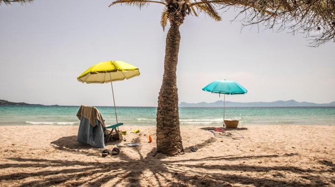 Zwei leere Stühle unter Sonnenschirmen stehen am 16. Juni 2021 bei hohen Temperaturen und Sonnenschein an einem Strand.