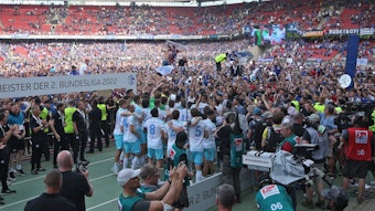 Der FC Schalke 04 feiert die Zweitliga-Meisterschaft, im Hintergrund stehen nach einem Platzsturm beim 1. FC Nürnberg Tausende Fans.