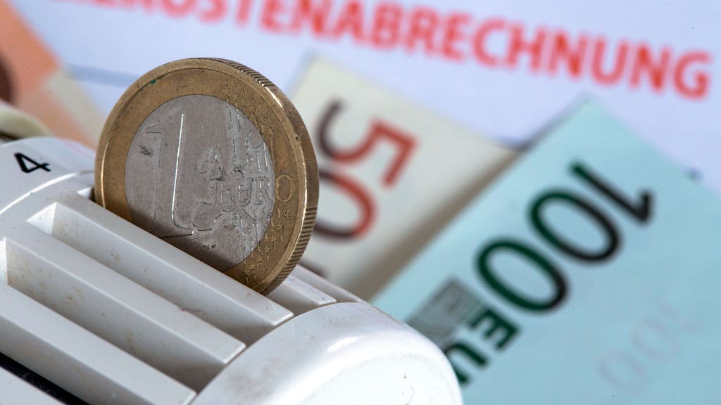 Eine Euromünze steckt am 04. Dezember 2014 in einem Heizungsthermostat, der auf einer Heizkostenabrechnung und Euro-Geldscheinen liegt.