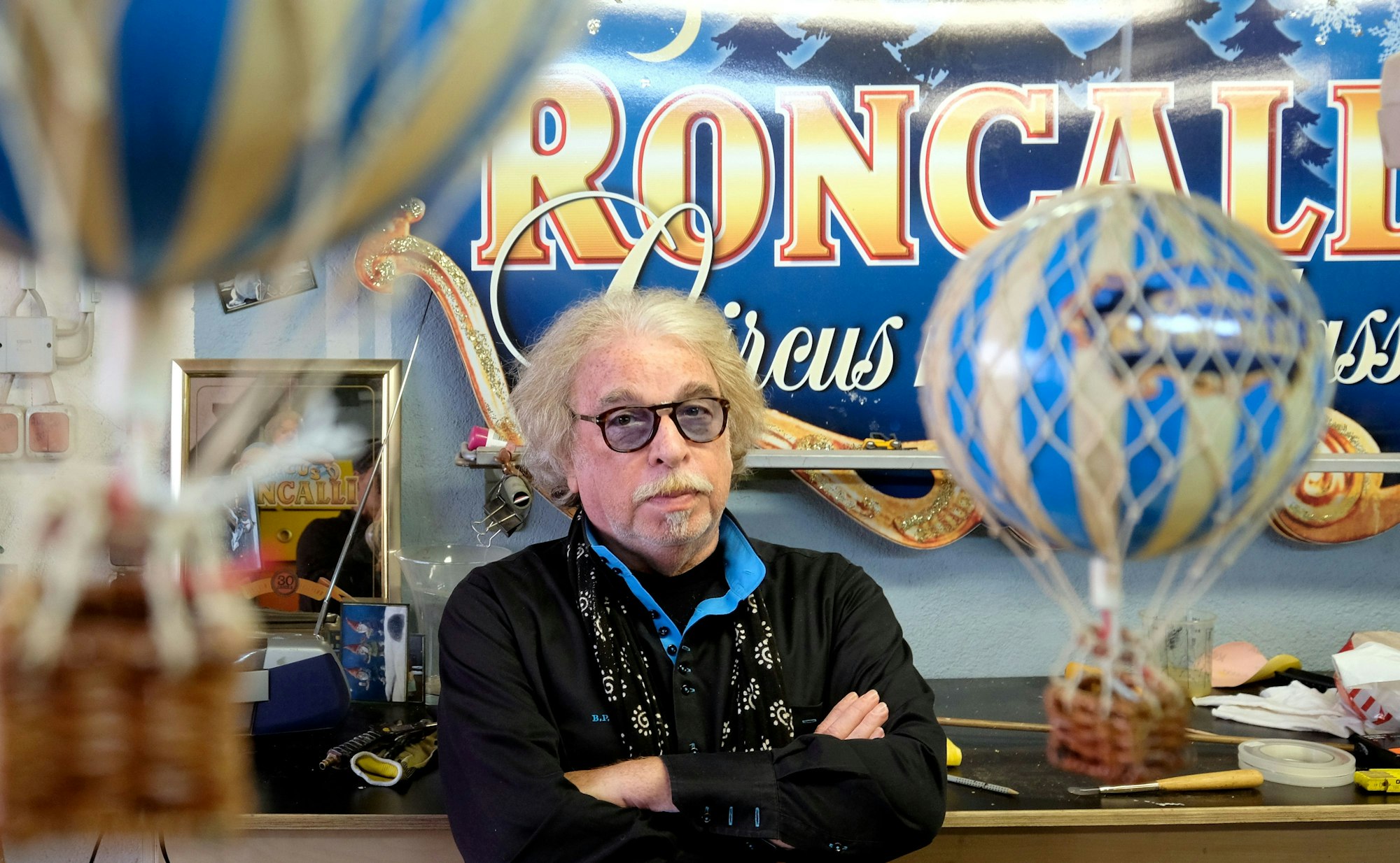 Bernhard Paul schaut vor einem Plakat des Circus Roncalli in die Kamera.