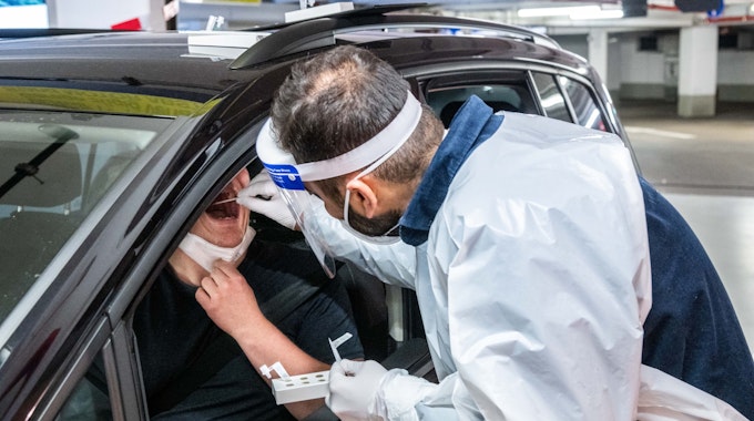 Ein Mitarbeiter eines Drive-In Testzentrums in Köln führt bei einem Autofahrer durch das geöffnete Fenster einen Schnelltest im Rachen durch.