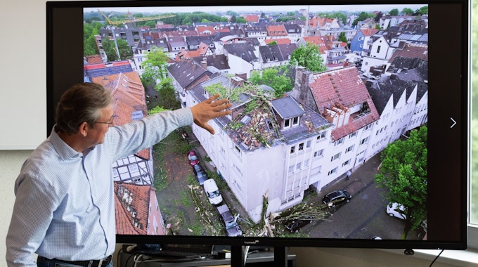 Der Bürgermeister von Paderborn, Michael Dreier, spricht bei einer Pressekonferenz am 21. Mai vor einem Display mit einem Schadensbild aus der Innenstadt, das zeigt, wie Bäume auf ein Hausdach geweht worden sind.