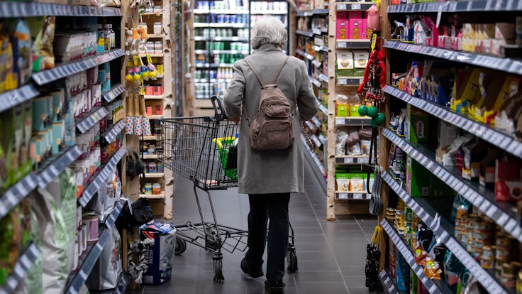 Eine Frau geht mit ihrem Einkaufswagen durch einen Supermarkt. Die hohen Preise von Lebensmitteln zwingen viele Menschen dazu, ihr Einkaufsverhalten zu ändern.